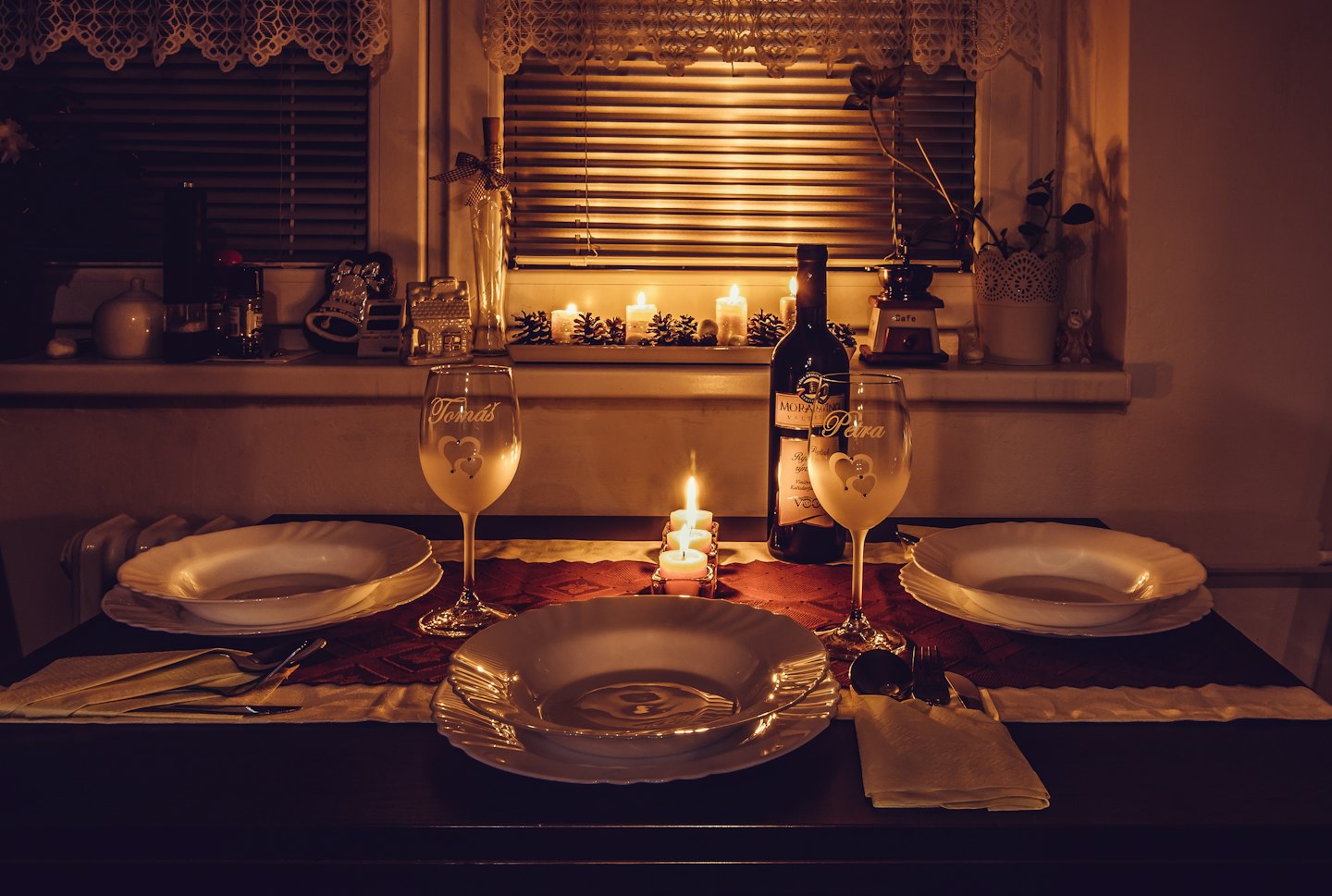 Dining table set for two with candles and wine glasses.