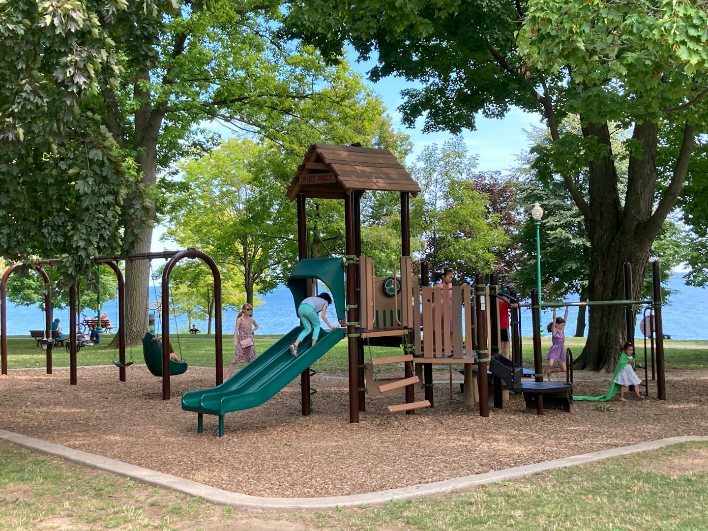 Children play on a playground structure with a woman watching.