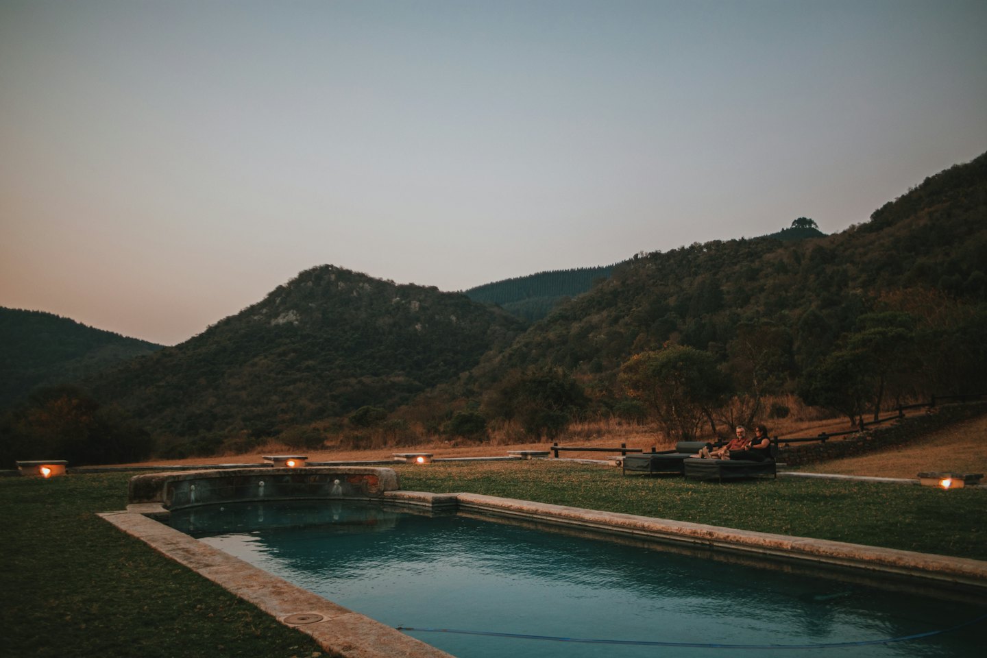 Couple relaxing by pool with mountains at twilight.