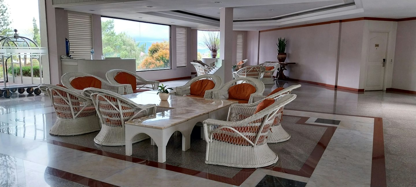 Hotel lounge with white wicker chairs and orange cushions around marble tables.